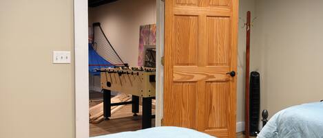 A bedroom with a wooden door, a futsal table, and a standing fan.