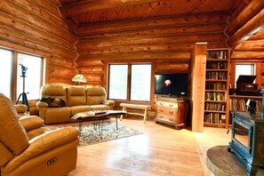 A log cabin interior with a sofa, recliner, television, bookshelf, and a fireplace. - Log cabin in the woods with views of Lake MI, Located in historic Cross Village (Harbor Springs)