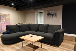 A modern living room with a sectional sofa, a wooden coffee table, and abstract art on the walls. - Log cabin in the woods with views of Lake MI, Located in historic Cross Village (Harbor Springs)
