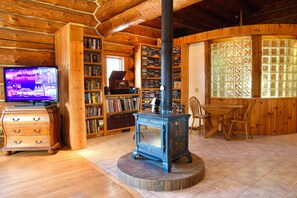 Ein gemütlicher Raum mit Holzvertäfelung, einem zentralen Kaminofen, einem Fernseher und Bücherregalen voller Bücher.