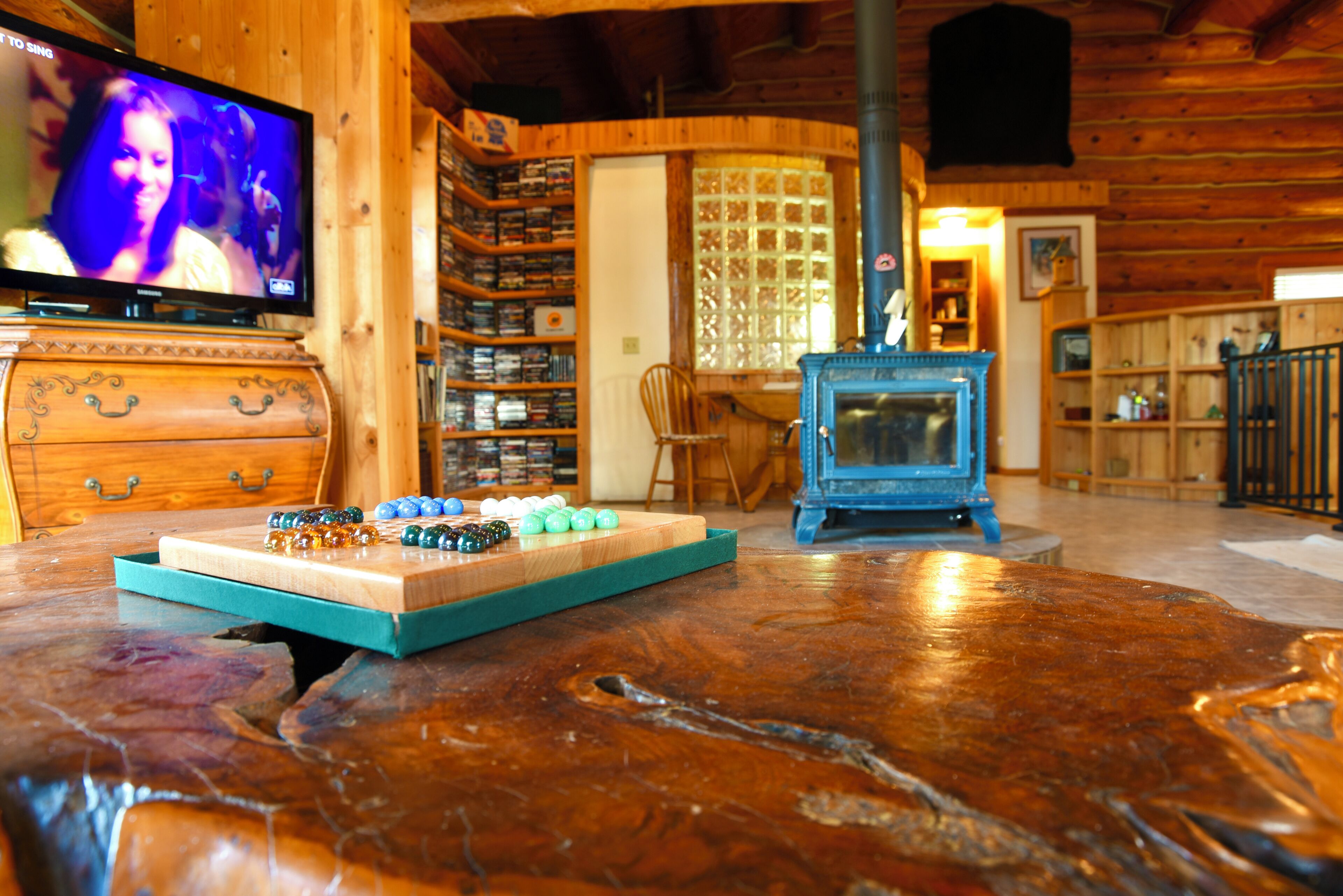 A wooden interior with a television, shelves with items, a blue fireplace, and a wooden table.