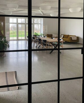 Ein geräumiges Zimmer mit großem Tisch und Stühlen, einer Couch und Blick durch ein Fenster.