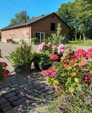 Ein Backsteinhaus mit Kiesauffahrt und Garten, bepflanzt mit verschiedenen Blumen und Pflanzen.