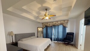 Een slaapkamer met een bed, een bureau, een stoel, een plafondventilator en een raam met gordijnen.
