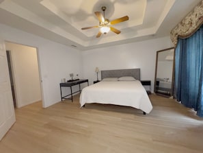 Une chambre à coucher comprenant un lit, un bureau, une table de chevet, un ventilateur de plafond et un miroir.