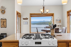 A kitchen with a gas stove, a view of a lake, and a dining area with a table and chairs.