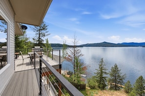 A wooden deck with outdoor furniture, overlooking a lake with mountains in the distance.