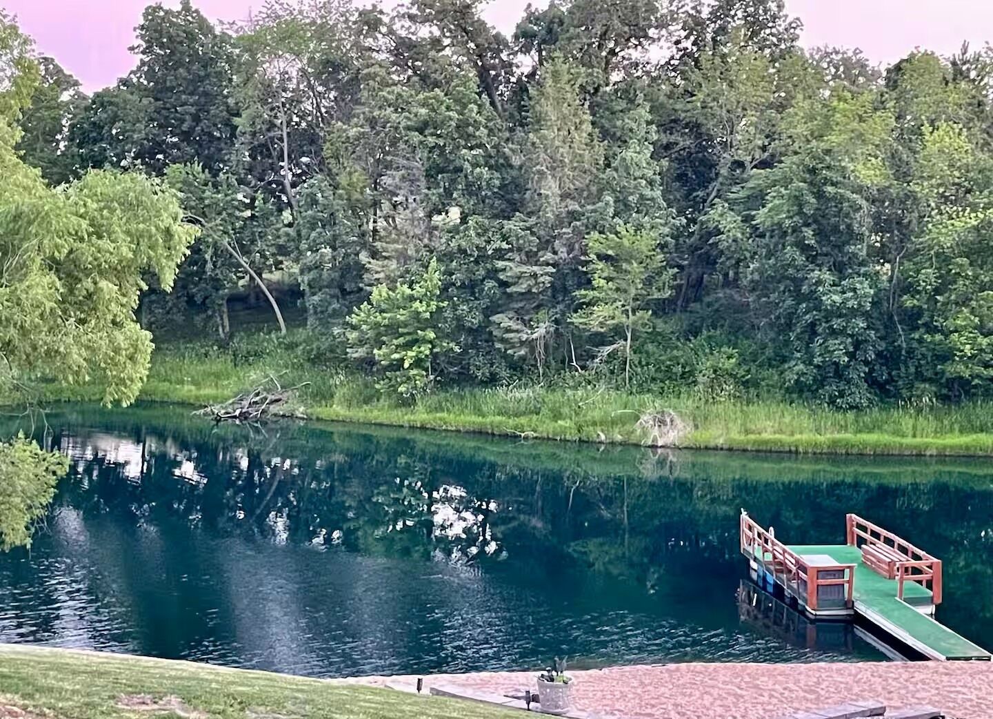 Um lago tranquilo com um píer de madeira e uma área gramada em primeiro plano.