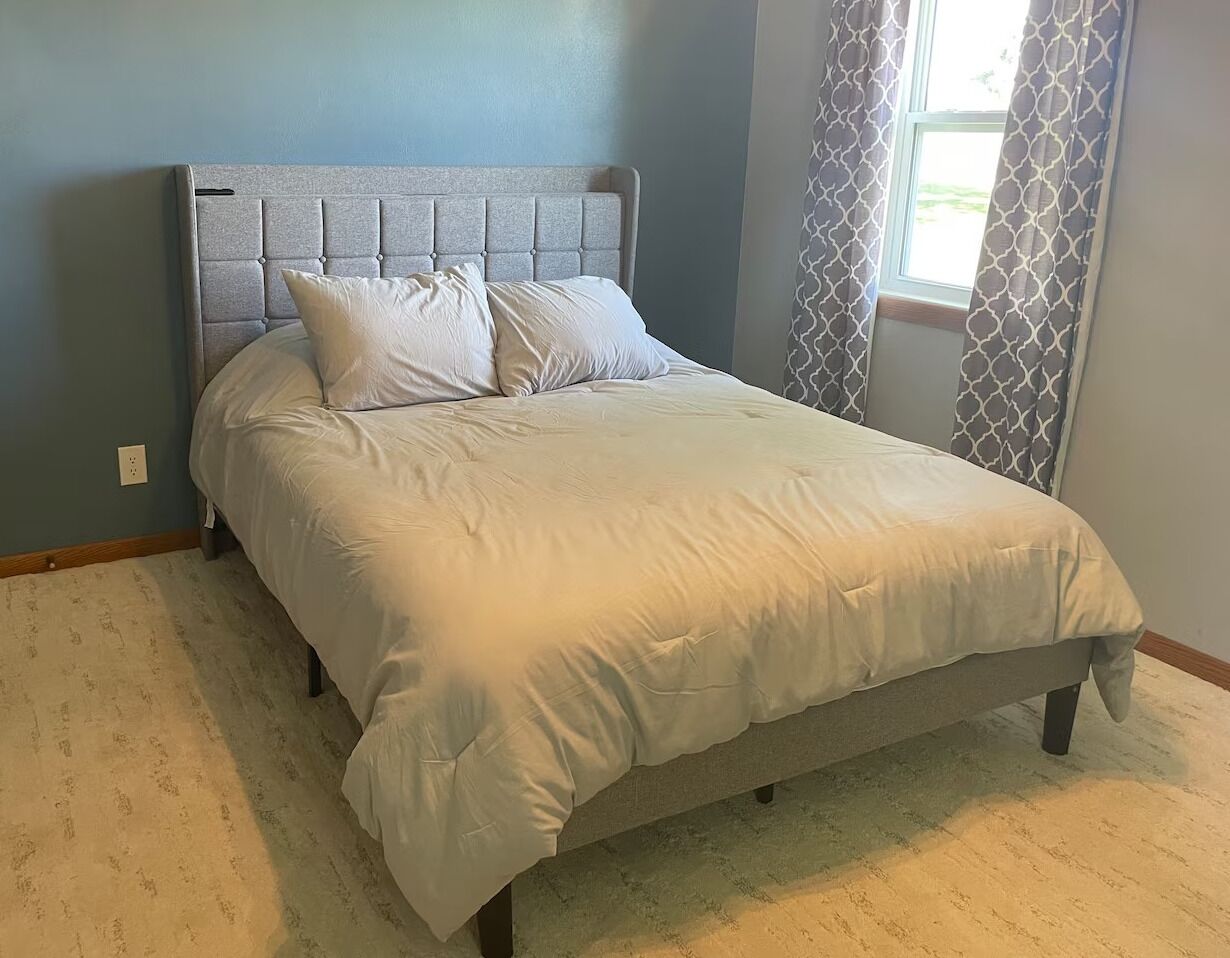 Une chambre à coucher avec un lit, une tête de lit et une fenêtre avec des rideaux.