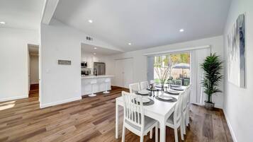 Un comedor amplio con una mesa larga, sillas blancas y una cocina al fondo.