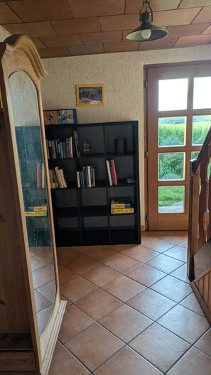 Une pièce avec un sol carrelé, un escalier en bois, une bibliothèque noire et un grand miroir.