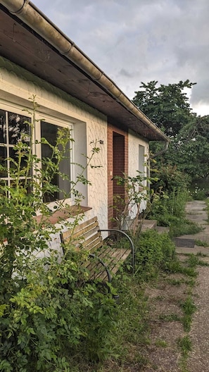 Una casa rústica con un banco de madera, una entrada de ladrillo y un camino de jardín que conduce a una puerta.