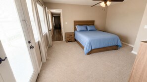 Une chambre à coucher comprenant un lit, une table de chevet, une tête de lit en bois, un ventilateur de plafond et une porte donnant sur une autre pièce.