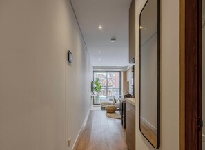 A hallway with a wooden floor, a large window with a view of buildings, and a door on the right. - NOK Modern 1BR near Usaquen & Unicentro (Bogota)