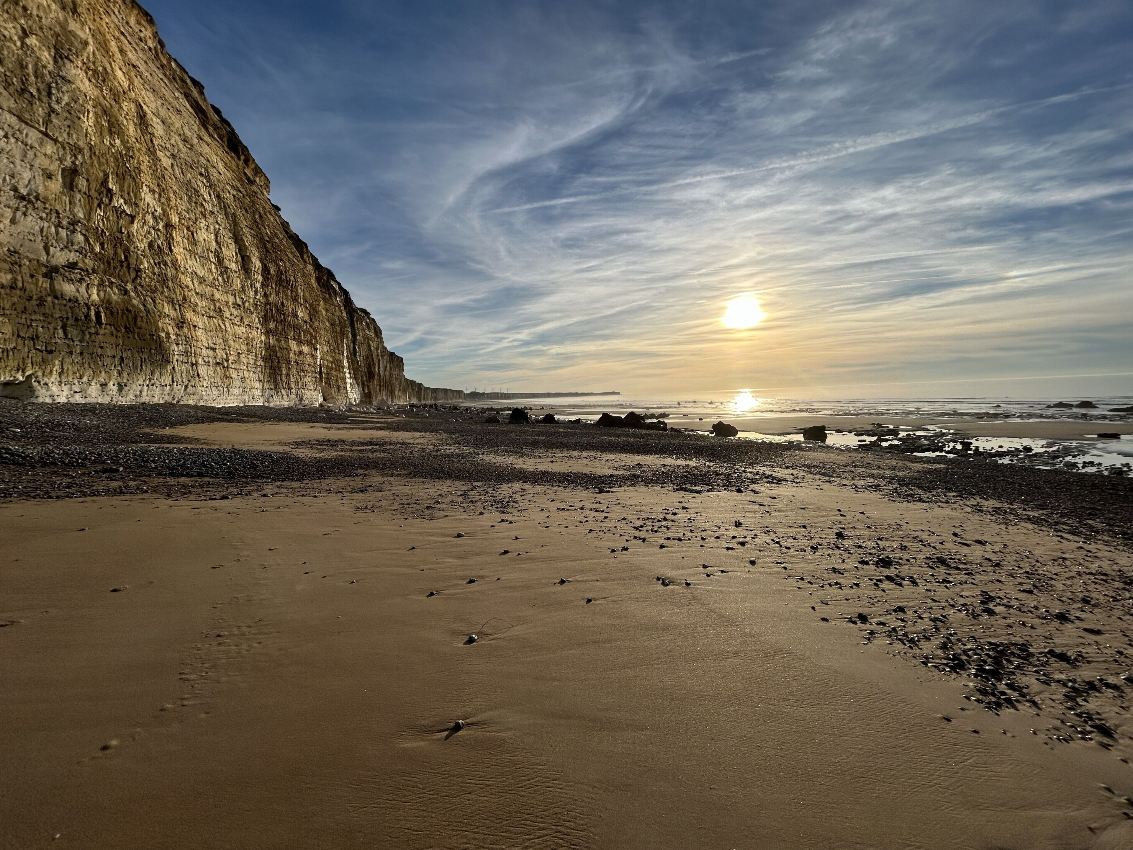 Une plage avec une grande falaise, un coucher de soleil et un ciel dégagé.