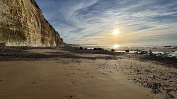 Une plage avec une grande falaise, un coucher de soleil et un ciel dégagé.