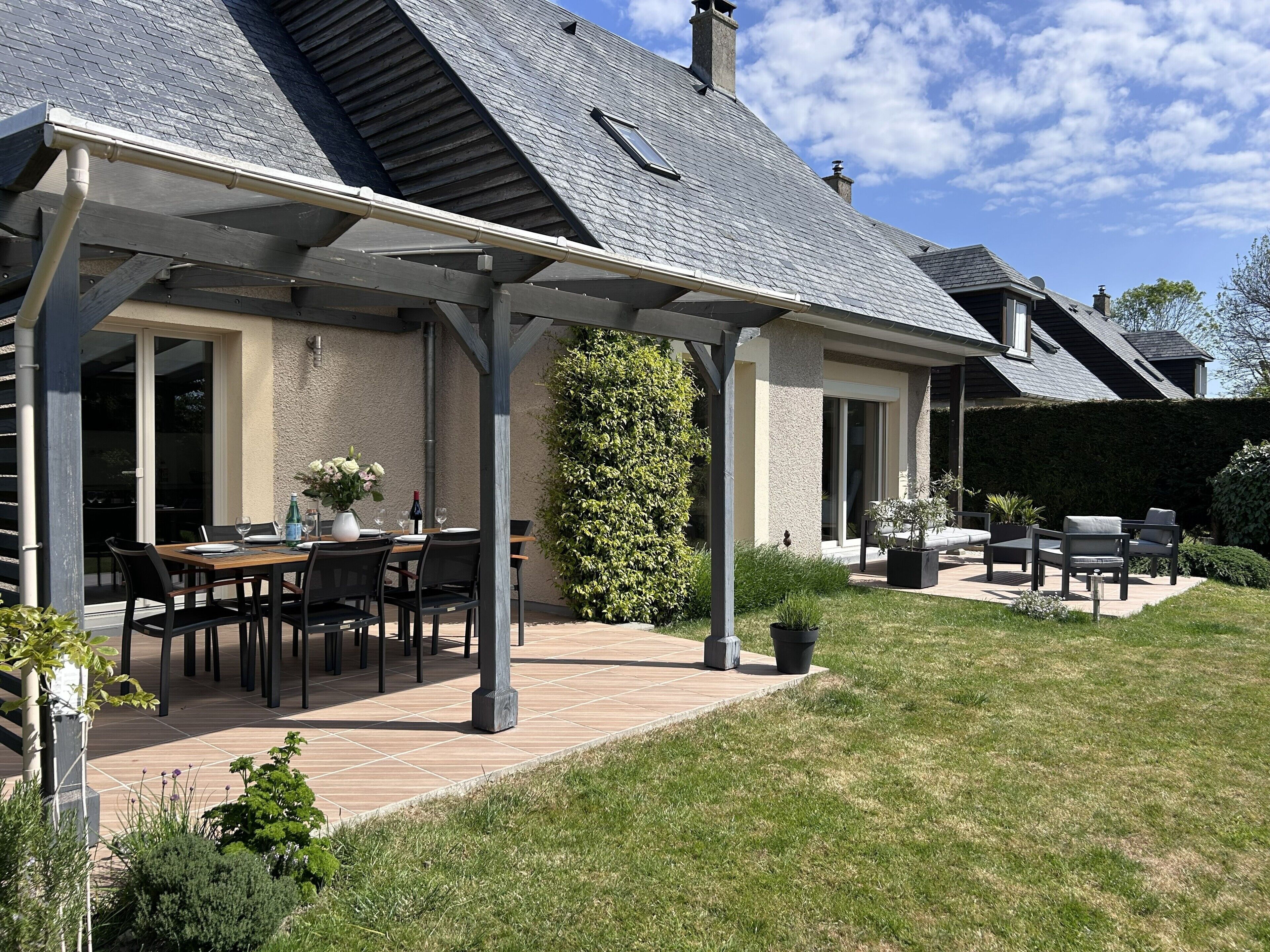 Un patio couvert avec des meubles d’extérieur, une table à manger et une haie.