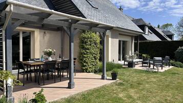Un patio couvert avec des meubles d’extérieur, une table à manger et une haie.