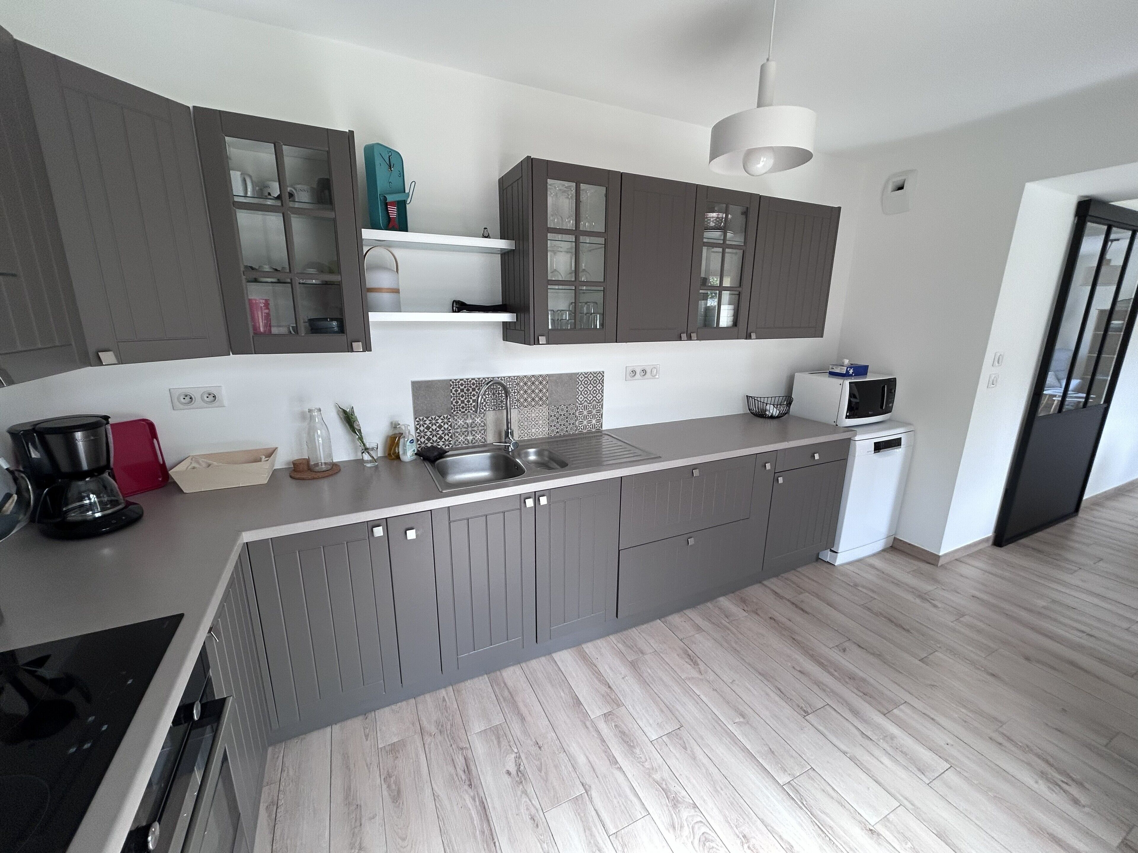 A modern kitchen with grey cabinets, a stainless steel sink, a coffee maker, and a microwave.