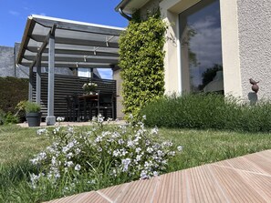 Un espacio de estar moderno al aire libre con una pérgola, una planta en maceta y un jarrón de pared.