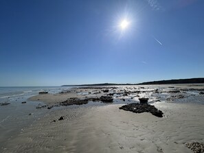 Una playa con rocas e huellas, cielos despejados y el sol brillando.