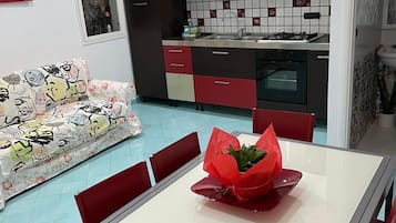 Ett modernt kök med röda och svarta skåp, kakel på väggen bakom arbetsbänken och en matplats med ett bord och stolar.