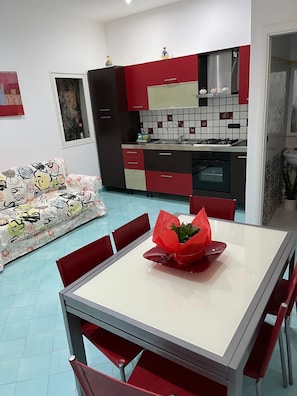 A modern kitchen with red and black cabinets, a tiled backsplash, and a dining area with a table and chairs. - THE HOUSE IN THE CATHEDRAL VIETRI SUL MARE (Vietri sul Mare)