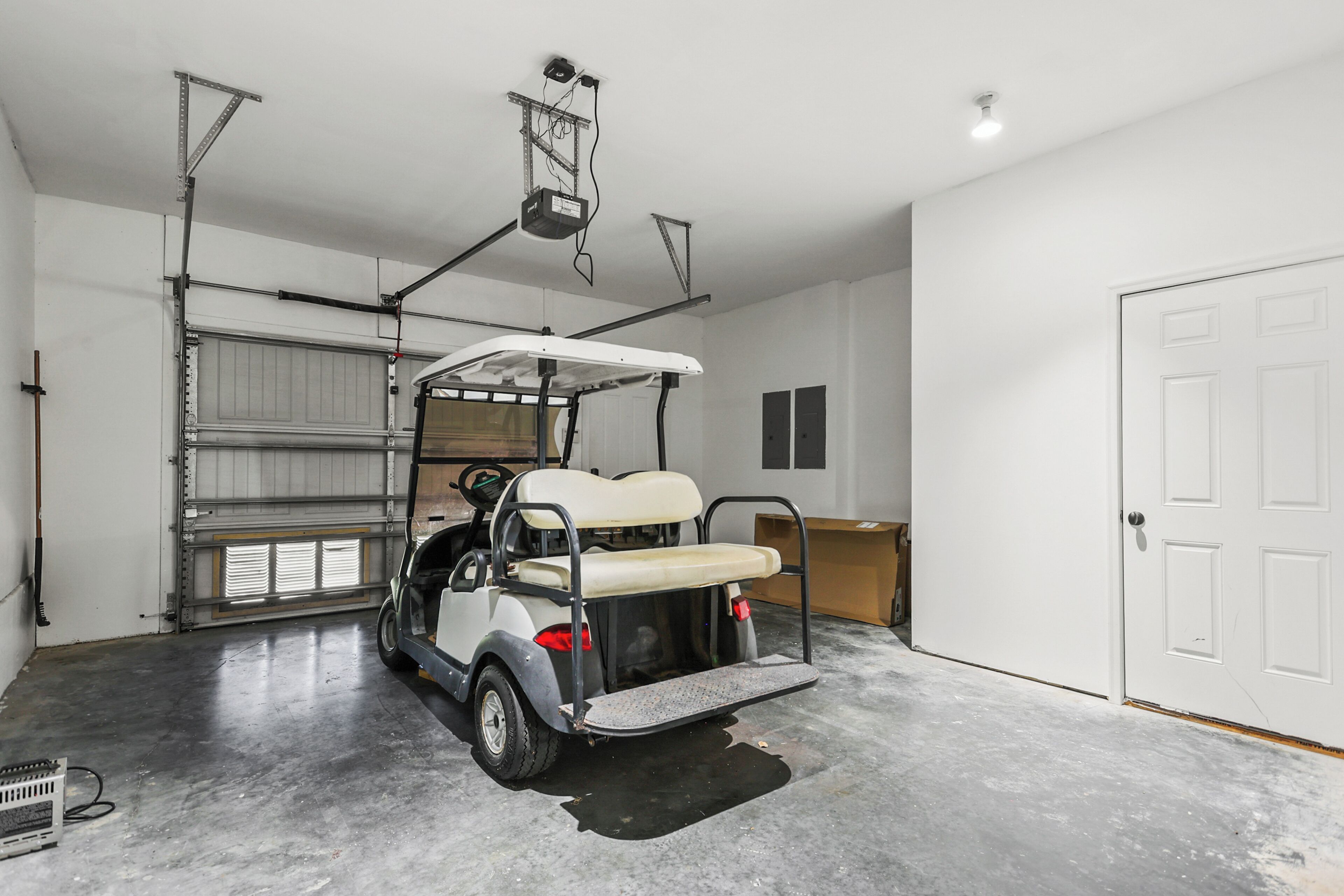 A garage with a golf cart, a closed garage door, and a white door.