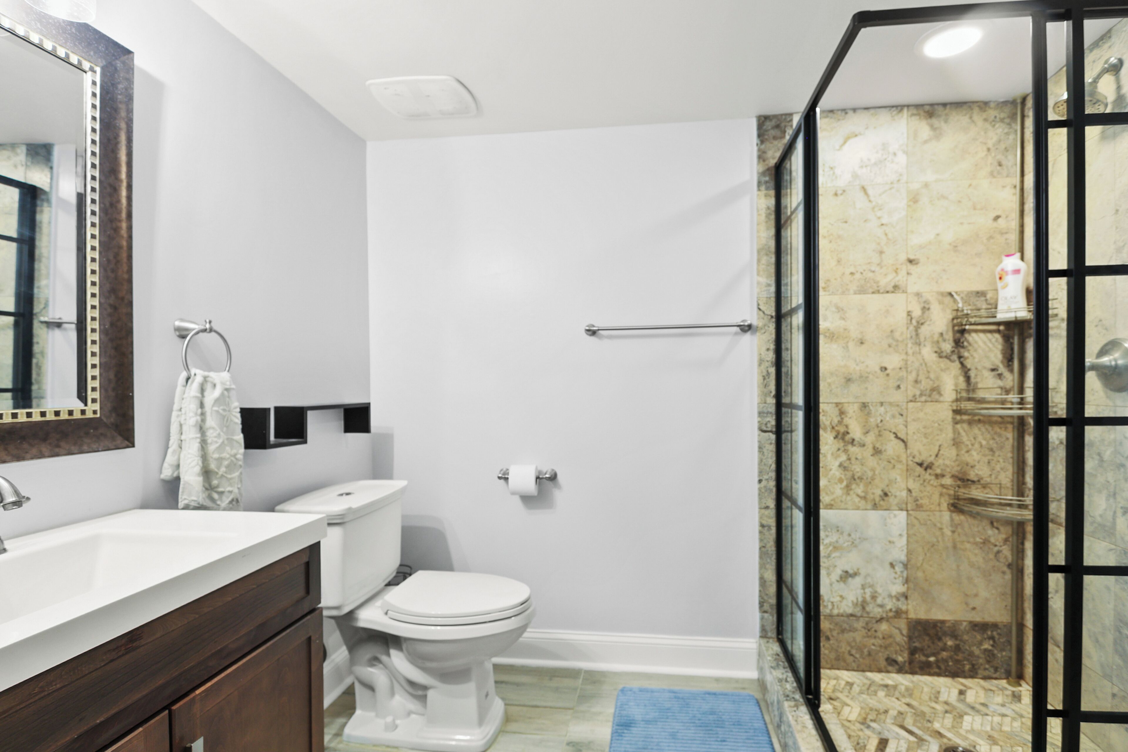 Une salle de bain avec des toilettes blanches, un lavabo avec un miroir et un espace douche doté d’une porte en verre.