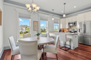 A modern kitchen with white cabinetry, stainless steel appliances, and a dining area with a round table and white chairs. - Retreat at Savannah Harbor 30+ Night Stay (Savannah)