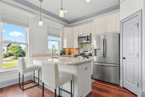 A kitchen with white cabinets, stainless steel appliances, and a large island with bar stools. - Retreat at Savannah Harbor 30+ Night Stay (Savannah)
