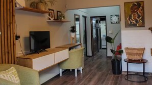 Ein modernes Wohnzimmer mit Fernseher, Holzmöbeln, einem Essbereich und einem Flur, der zu weiteren Räumen führt.