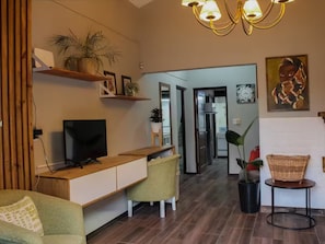 Una sala de estar moderna con televisor, muebles de madera, una zona de comedor y un pasillo que conduce a otras habitaciones.