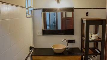 Ein Badezimmer mit schwarzem Waschtisch, einem beige-farbenen Waschbecken, einem Spiegel und einem Ablagebereich für Toilettenartikel.
