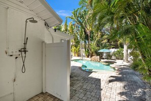 A white building with a shower, a pool, and palm trees. - The Crescent by Duncan Real Estate (Anna Maria)