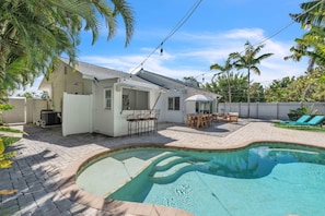 A backyard with a swimming pool, a covered patio with outdoor furniture, and a white house with a fenced yard. - The Crescent by Duncan Real Estate (Anna Maria)