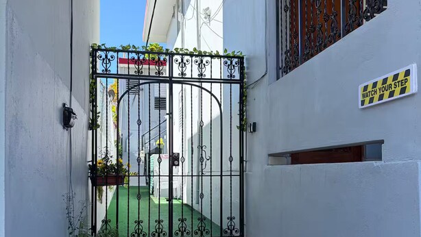 Une entrée ferm ée par un portail en métal, un petit escalier et une plaque fixée au mur.