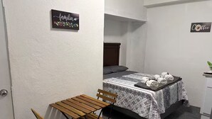 Une petite pièce avec un lit, une table et des chaises, une pancarte indiquant « familia », et une autre pancarte indiquant « Café ».