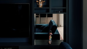 Una sala de estar moderna con un televisor de pantalla plana grande, muebles azul oscuro y objetos decorativos en estanterías.
