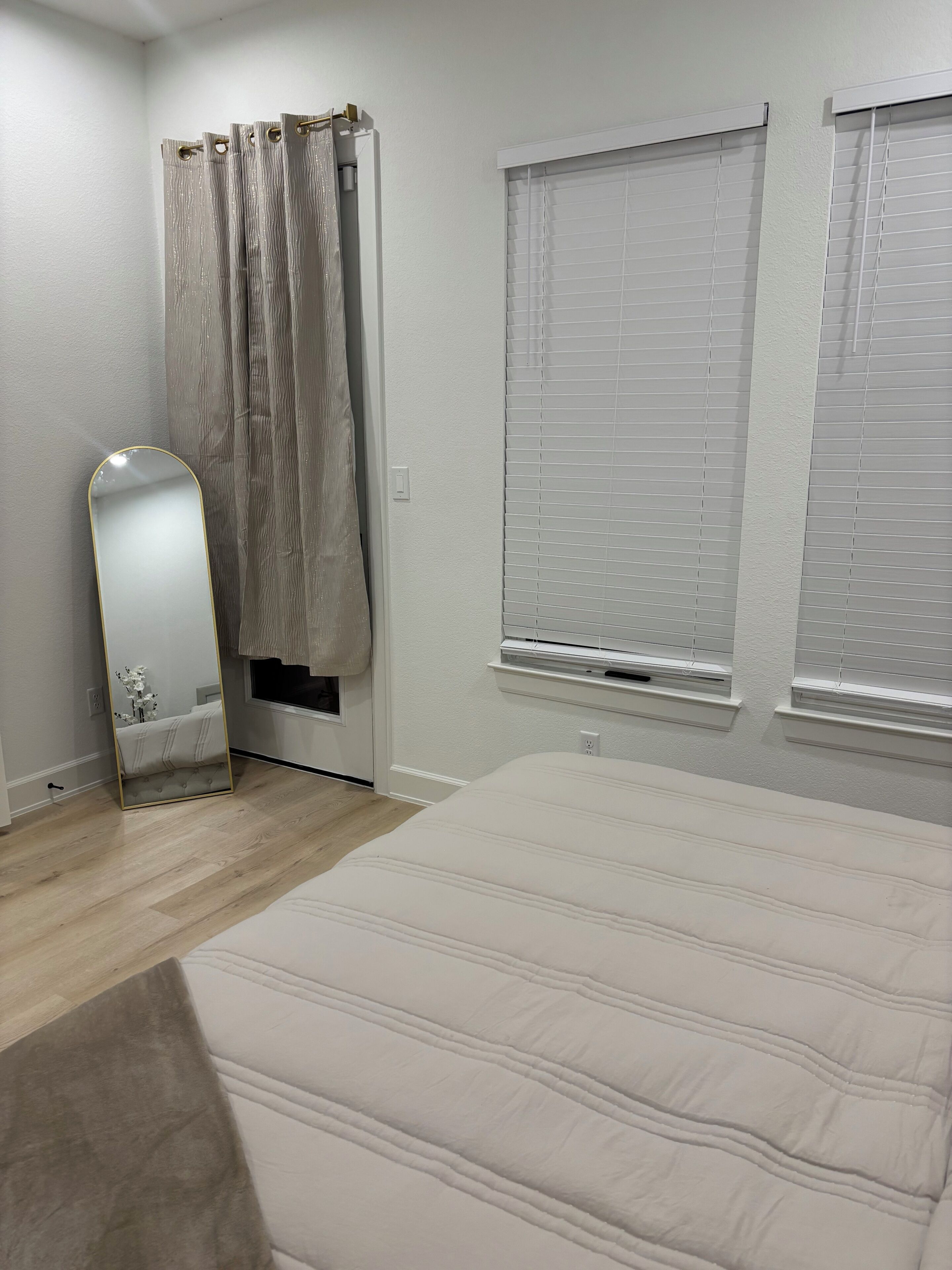A bedroom with a bed, a mirror, curtains, and two windows with blinds.