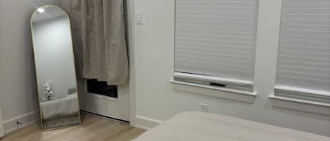 A bedroom with a bed, a mirror, curtains, and two windows with blinds.