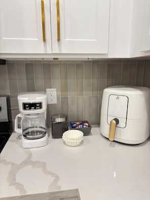 A kitchen with white cabinets, a coffee maker, a toaster, a bowl of snacks, and a small container.