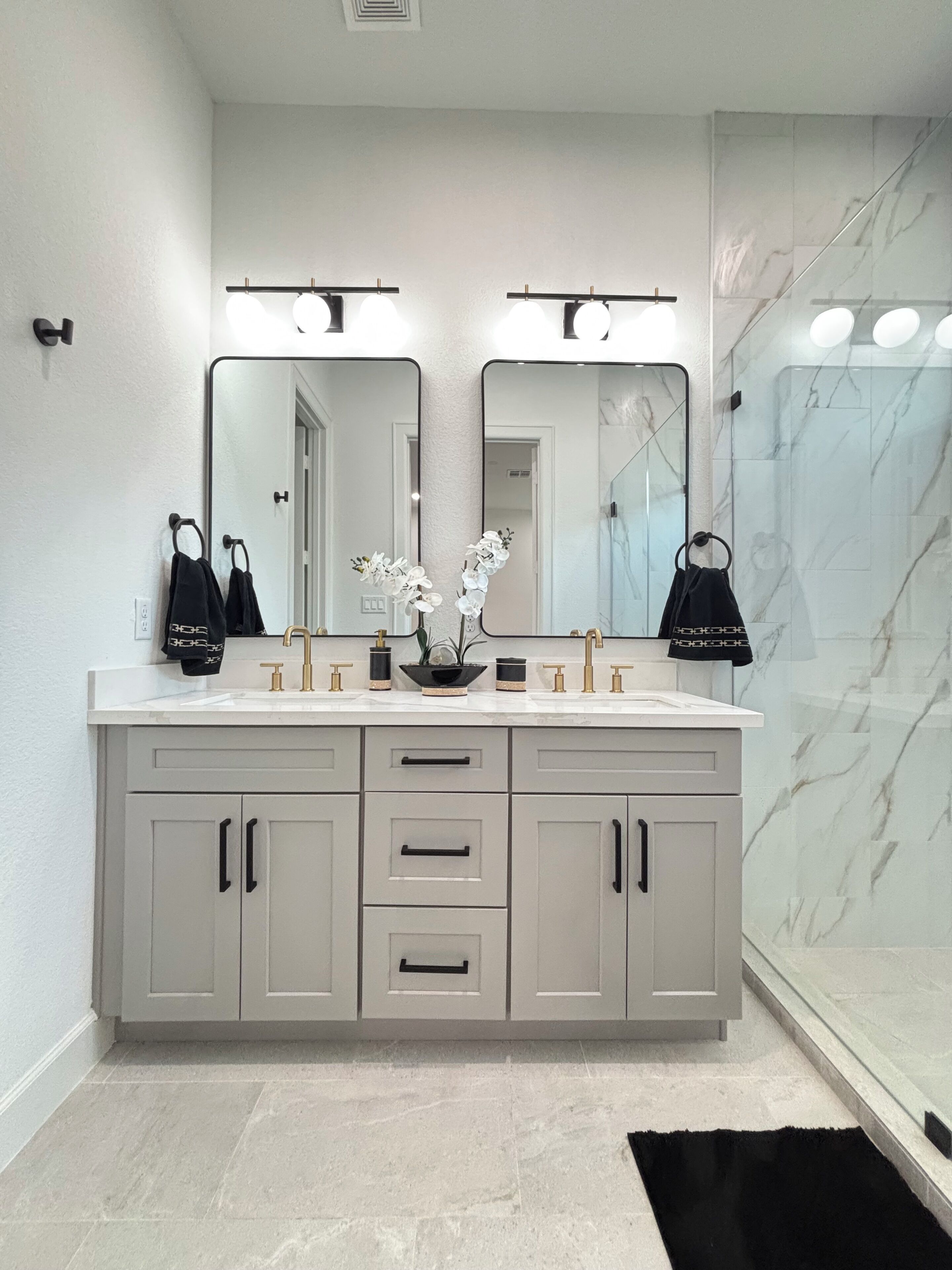 A modern bathroom with a double vanity, marble backsplash, and a black rug.