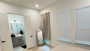 Ein Schlafzimmer mit Bett, ein Badezimmer mit Spiegel und ein Fenster mit Jalousien.