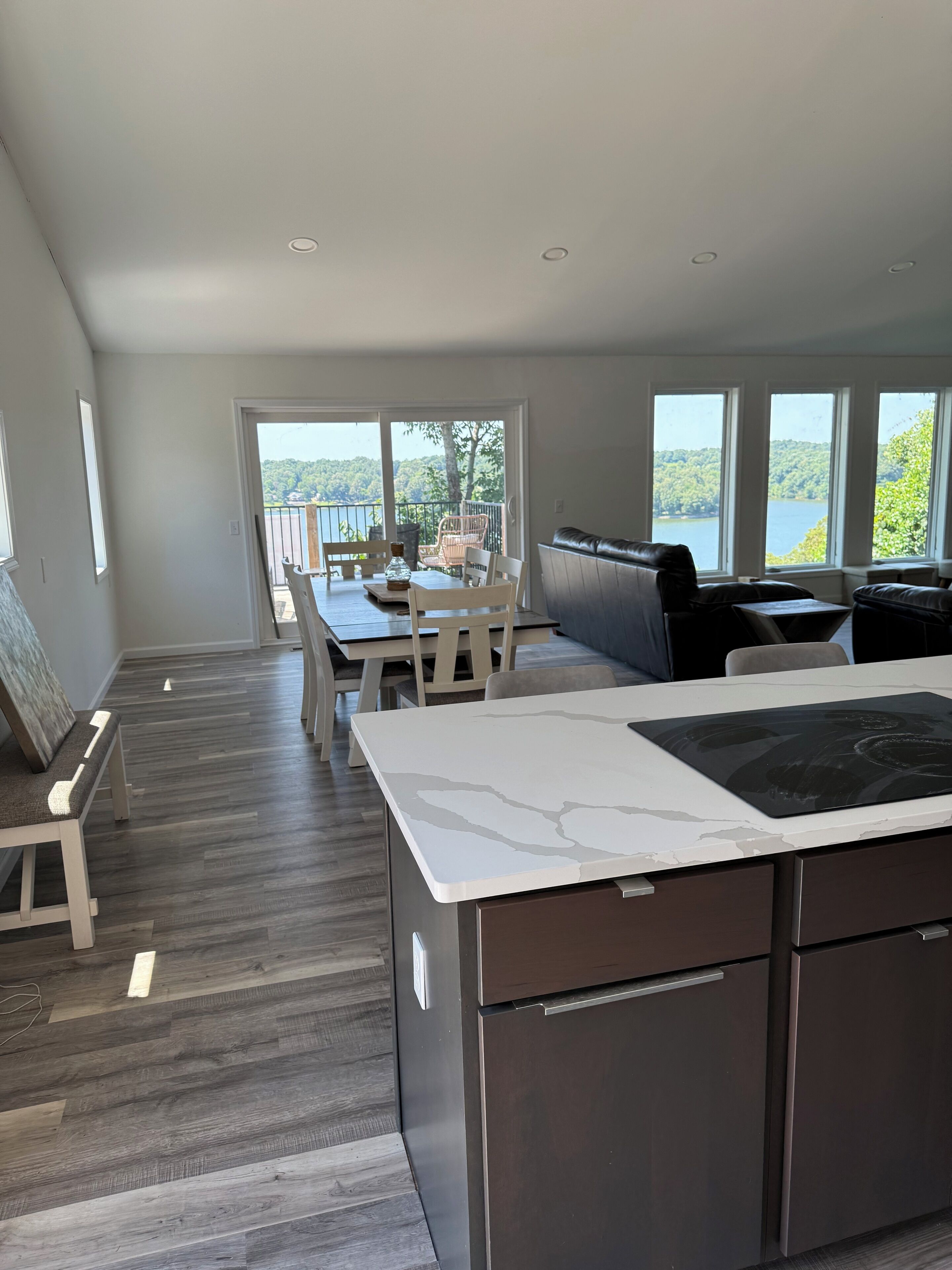 A modern kitchen with a marble countertop, dark cabinetry, and a dining area with a view of a lake.