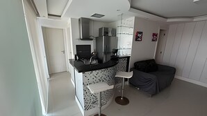 Una cocina compacta con electrodomésticos modernos, una zona de comedor con un taburete de bar y un sofá gris.