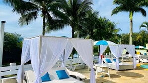 Un área junto a la piscina con toldos blancos y sillas de descanso.