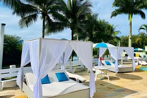 Un área junto a la piscina con toldos blancos y sillas de descanso.