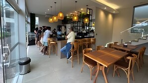 Un café moderno con mesas y sillas de madera, iluminación colgante y una zona de bar.