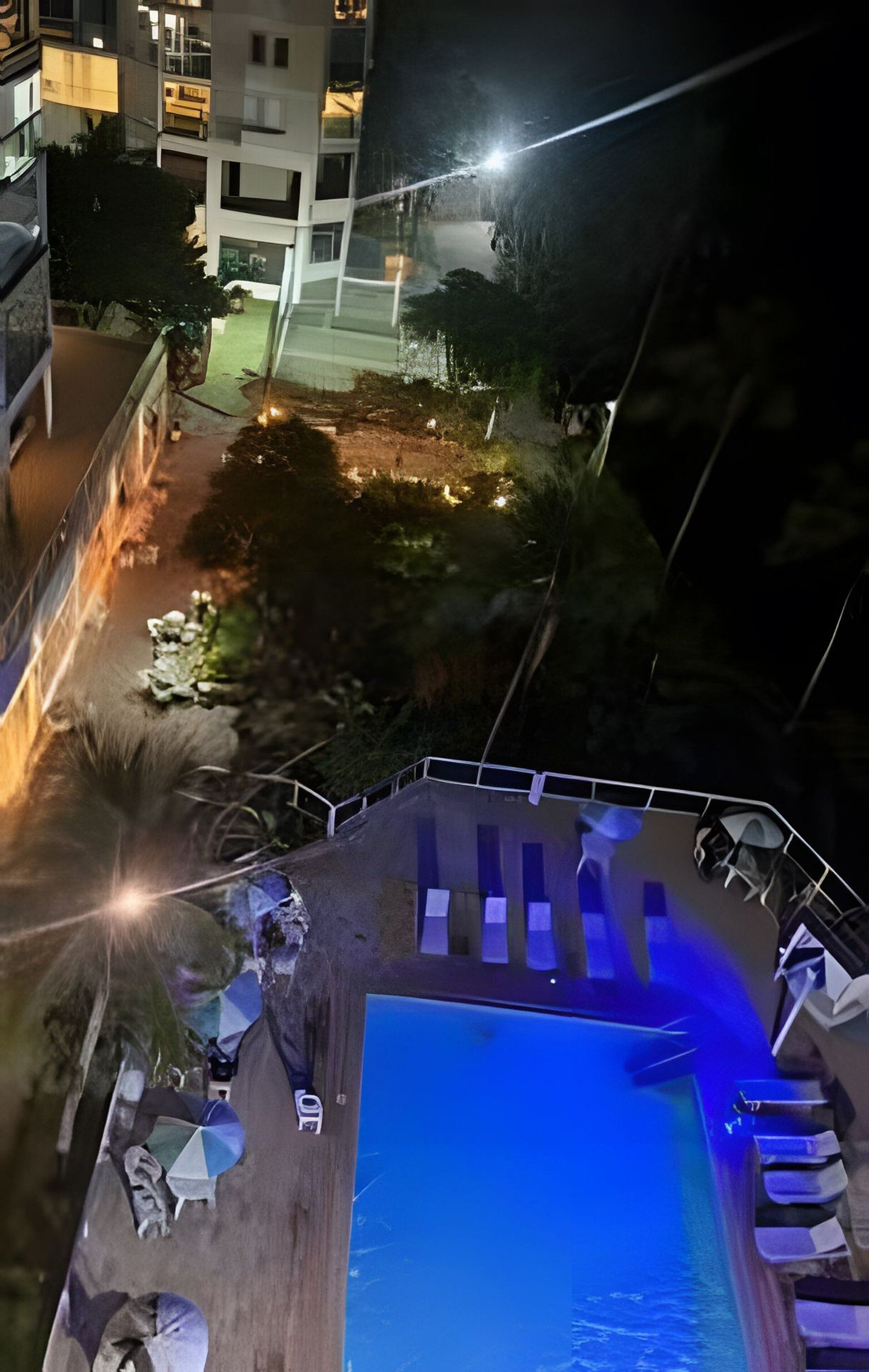 A rooftop pool with lounge chairs and a view of the cityscape at night.